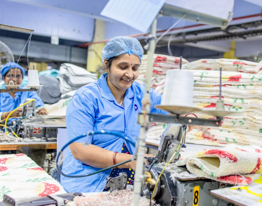 Inside view of Divine Uniform's bulk stitching unit in New Delhi showing rows of industrial sewing machines and stacked fabric rolls ready for mass production